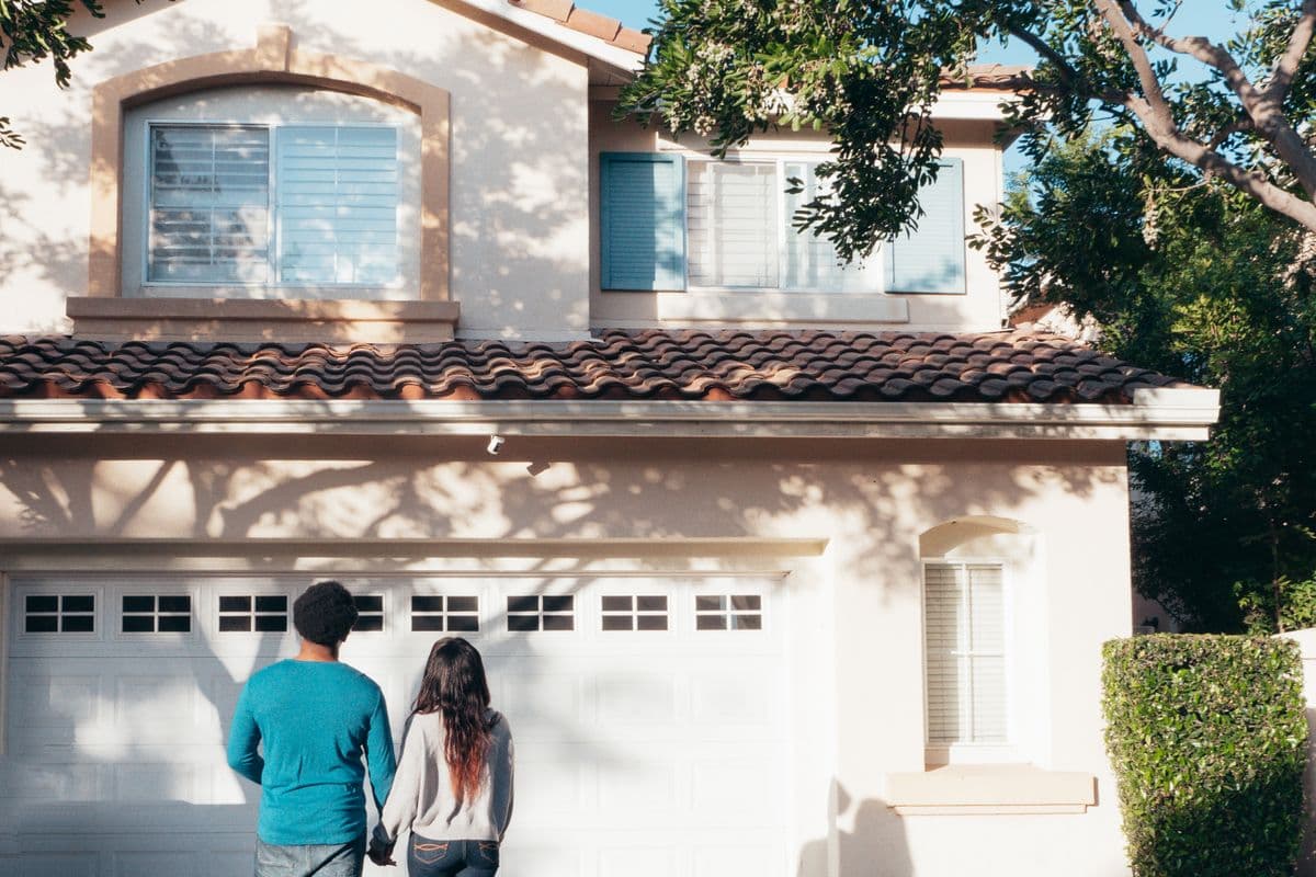 A couple hand in hand, seen from behind, looking at the house in front of them